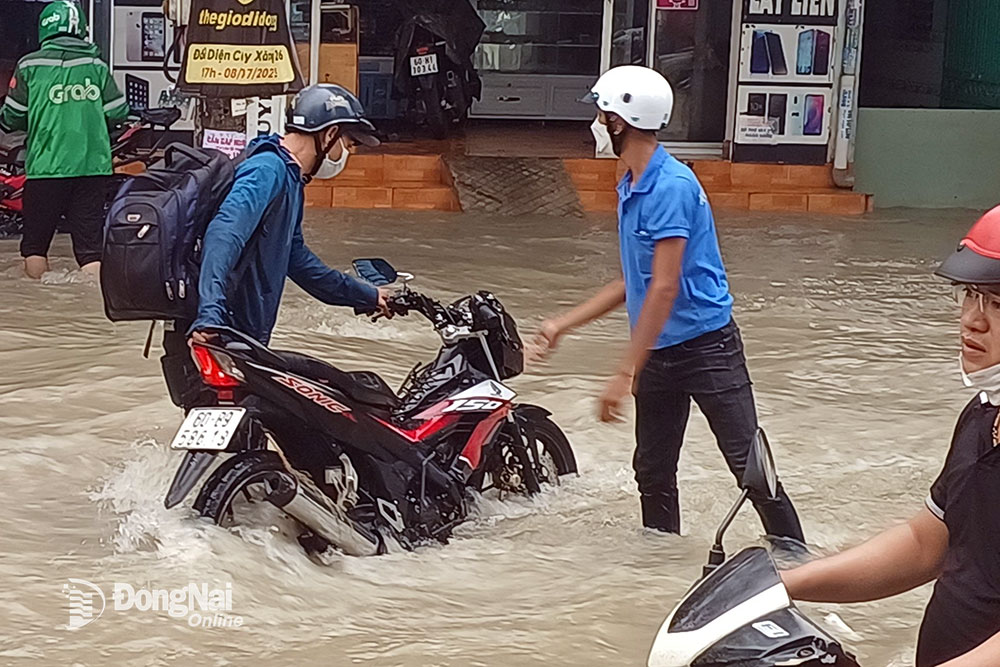 Người đi xe máy phải hỗ trợ nhau khiêng chiếc xe qua điểm ngập vì sợ chết máy. Ảnh: Thành Nhân