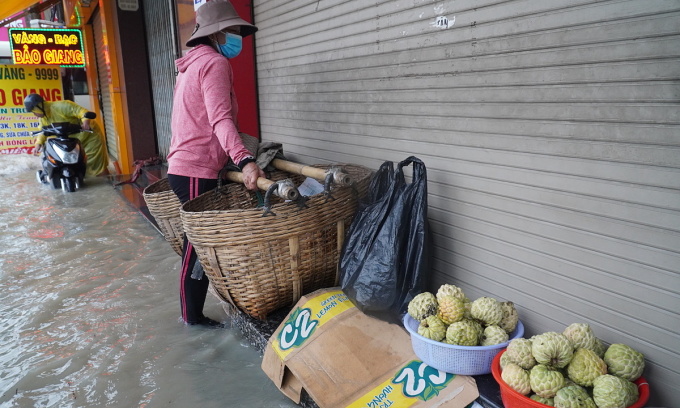 Một tiểu thương bán trái cây vỉa hè chật vật di dời hàng hóa do nước dâng cao bất ngờ. Ảnh: Phước Tuấn