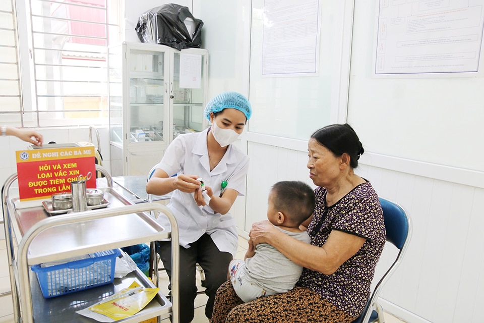 Cán bộ y tế TYT xã Minh Cường, huyện Thường Tín thông tin cho gia đình về loại vaccine được sử dụng để tiêm phòng cho trẻ trước khi tiêm.