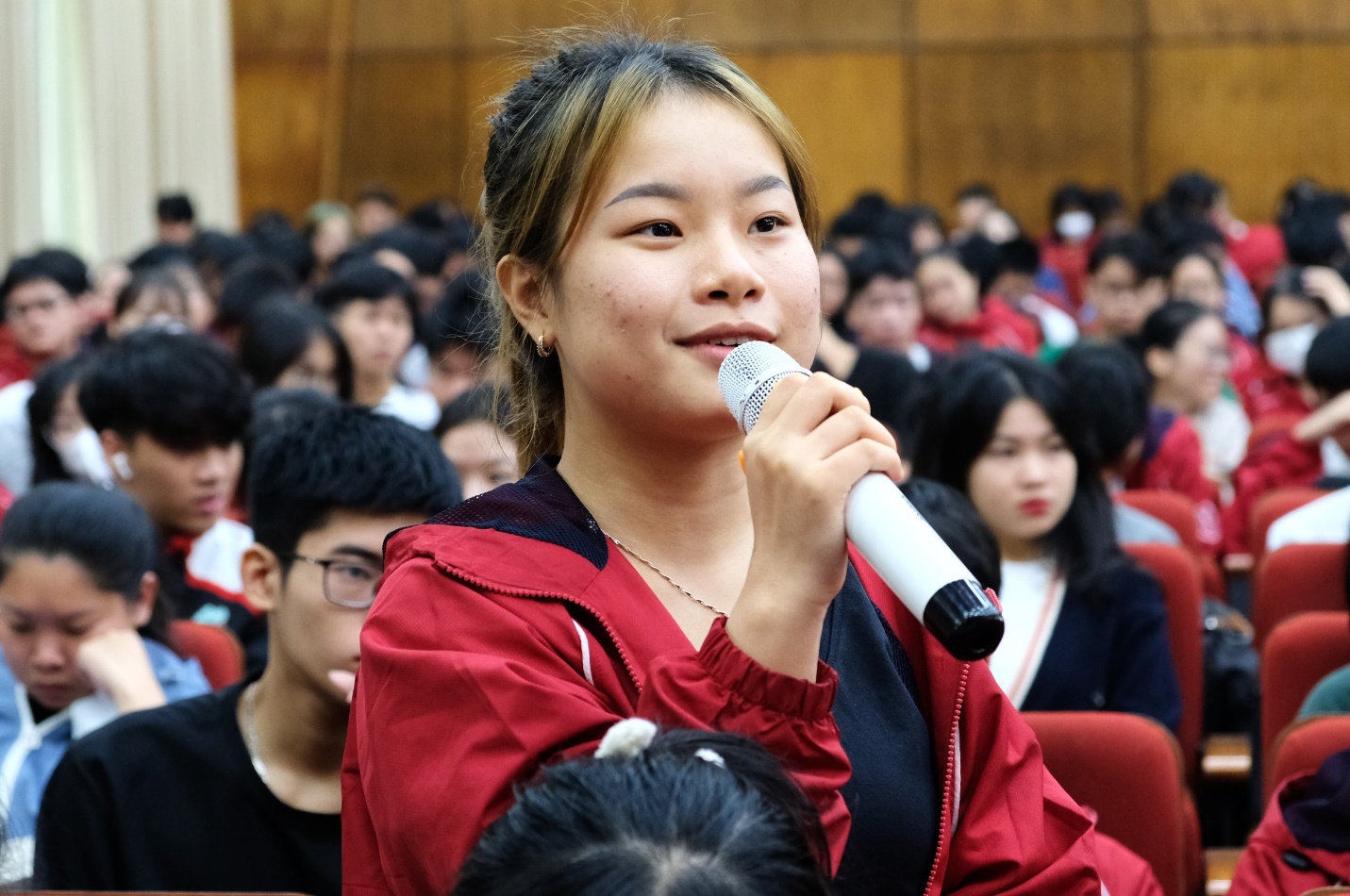 A person holding a microphone in front of a crowd  Description automatically generated