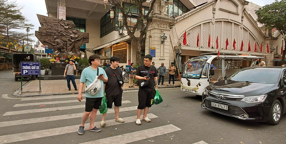 Khách du lịch đợi xe trung chuyển từ điểm đón trước cổng chợ Đồng Xuân di chuyển vào khách sạn trong phố cổ. Ảnh: Hoài Nam